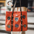 Person holding an orange tote bag with patches in an urban setting